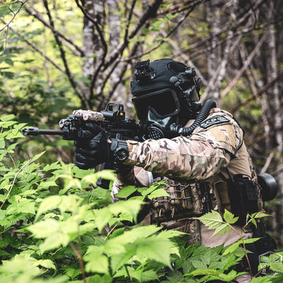 3/4 shot of a soldier in camouflaged tactical equipment, wearing a CM-8M gas mask and shouldering an assault rifle. 